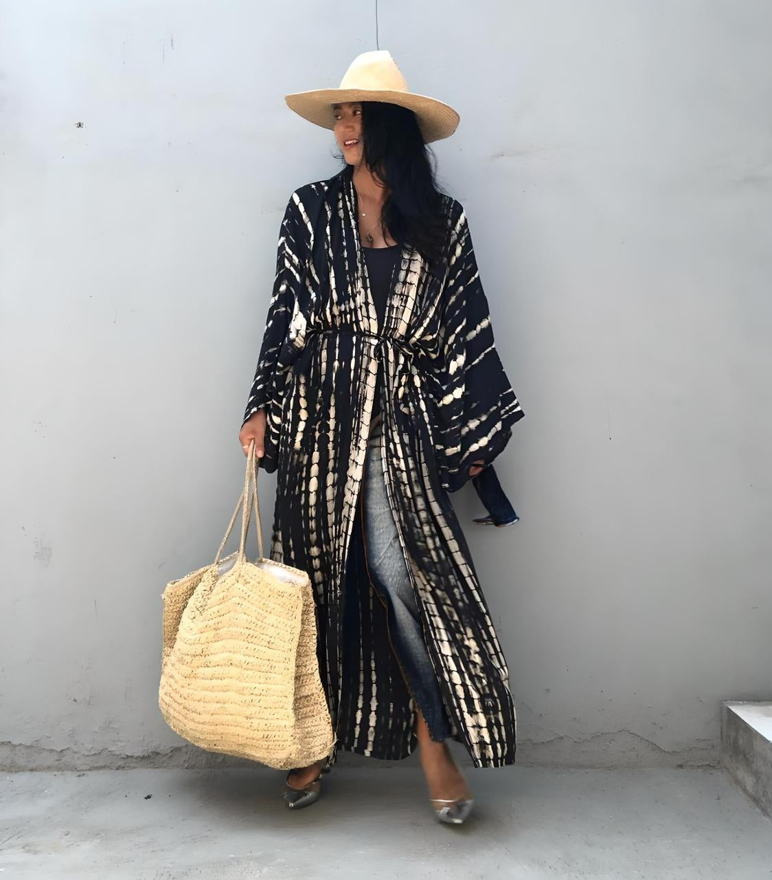Woman wearing a long black and white patterned coat, holding a beige bag against a plain background